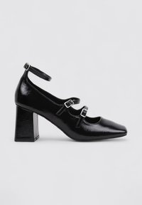 Zapatos de charol negros con tacón cuadrado y puntera almendrada, que presentan dos correas de tobillo con hebillas y una textura suave y brillante.