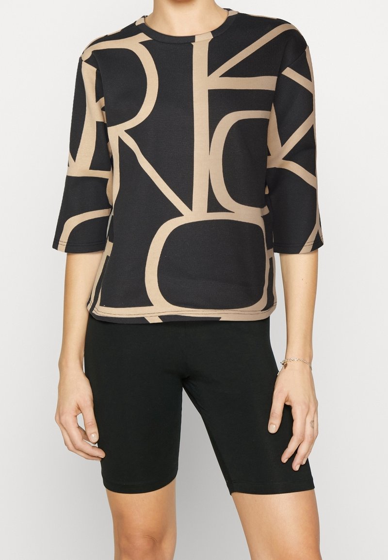 Top nero e beige con motivo a fantasia e maniche a tre quarti, caratterizzato da forme astratte, abbinato a pantaloni corti neri aderenti. Tessuto liscio, design casual.
