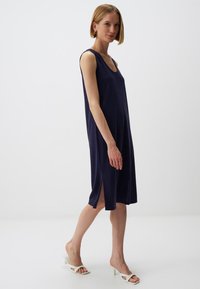 Granatowa sukienka bez rękawów o luźnym kroju, do kolan, z bocznymi rozcięciami i okrągłym dekoltem. Miękka tkanina o gładkiej fakturze.