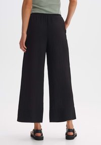 Black wide-leg pants with a textured fabric featuring vertical pleats, an elastic waistband, and side pockets. Worn with black sandals.