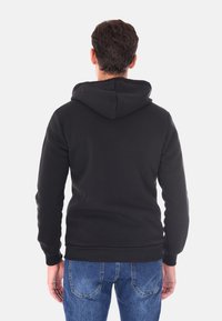 Felpa nera con vista posteriore, dotata di cappuccio con cordino e polsini a coste. Abbinata a jeans in denim, che mostrano un design e una vestibilità casual.