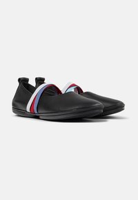 Zapatos de cuero negro con puntera redondeada, que presentan un diseño de doble tira elástica en rojo y azul claro. Textura suave y estilo minimalista.