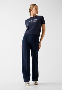 Granatowy bawełniany T-shirt z białym logo, zestawiony z dopasowanymi granatowymi spodniami. Oba elementy cechują się gładką teksturą i nowoczesną sylwetką.