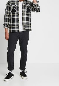 Czarna i biała flanelowa koszula w kratę z żółtymi akcentami, dwie kieszenie na piersi, pod spodem biała koszulka, ciemne dżinsy i czarne buty.