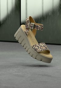 Sandale à plateforme épaisse avec des brides beige et marron à imprimé léopard et une boucle argentée réglable sur un fond gris neutre.