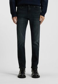 Jeans de denim oscuro con un ajuste slim, con un desvanecimiento sutil, diseño clásico de cinco bolsillos y combinados con botas negras de cordones.