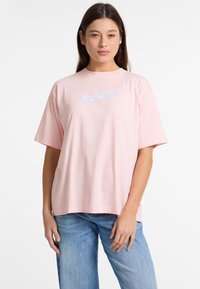 Lyserød bomulds T-shirt med rund hals og korte ærmer. Har et broderet "Guess Jeans" logo i lyseblå på forsiden.