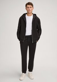 Czarny sportowy dres z białymi detalami, składający się z rozpinanej bluzy z kapturem oraz zwężanych spodni. Uzupełniony białymi trampkami.