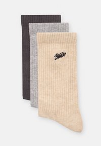 Tre par ribbede sokker i sort, grå og beige med et lille sort logo. Hver sok har en glat overflade og en medium højde.