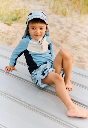 Conjunto de ropa de baño con protección solar que incluye una camiseta de manga larga azul claro y pantalones cortos azules con estampados marinos. Incluye un sombrero a juego.