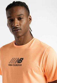 Bright orange athletic t-shirt with a textured fabric, featuring a black “new balance” logo on the chest. Short sleeves and round neckline.