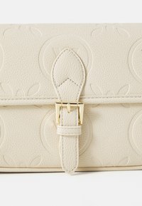 Ivoren gestructureerde leren tas met verhoogde cirkelpatronen, voorzien van een goudkleurige sluiting en een bijpassende strap.