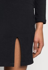 Czarna, dopasowana sukienka z rozcięciem tuż nad kolanem. Wykonana z miękkiej bawełny, z rękawami 3/4 i gładką teksturą.