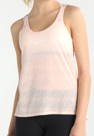Femme portant un haut de sport sans manches Nike rose clair avec un motif répétitif discret du texte "nike" et un pantalon noir.