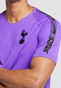Purple athletic shirt featuring a black Spurs logo on the chest and bold "SPURS" text on the sleeve. Smooth texture, short sleeves.