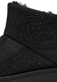 Bottine en velours noir avec une surface texturée ornée de clous noirs dispersés. Semelle en caoutchouc lisse et col doux en fourrure.