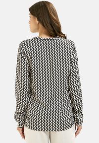 Langärmlige Bluse mit einem schwarz-cremefarbenen geometrischen Hahnentrittmuster, abgerundetem Ausschnitt und geknöpften Manschetten. Glatte Stoffstruktur.