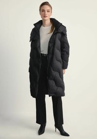 Czarna kurtka puchowa z kapturem, z pikowanym wzorem i zapięciem na zamek. Noszona na lekkiej bluzce, zestawiona z dopasowanymi spodniami i szpilkami.