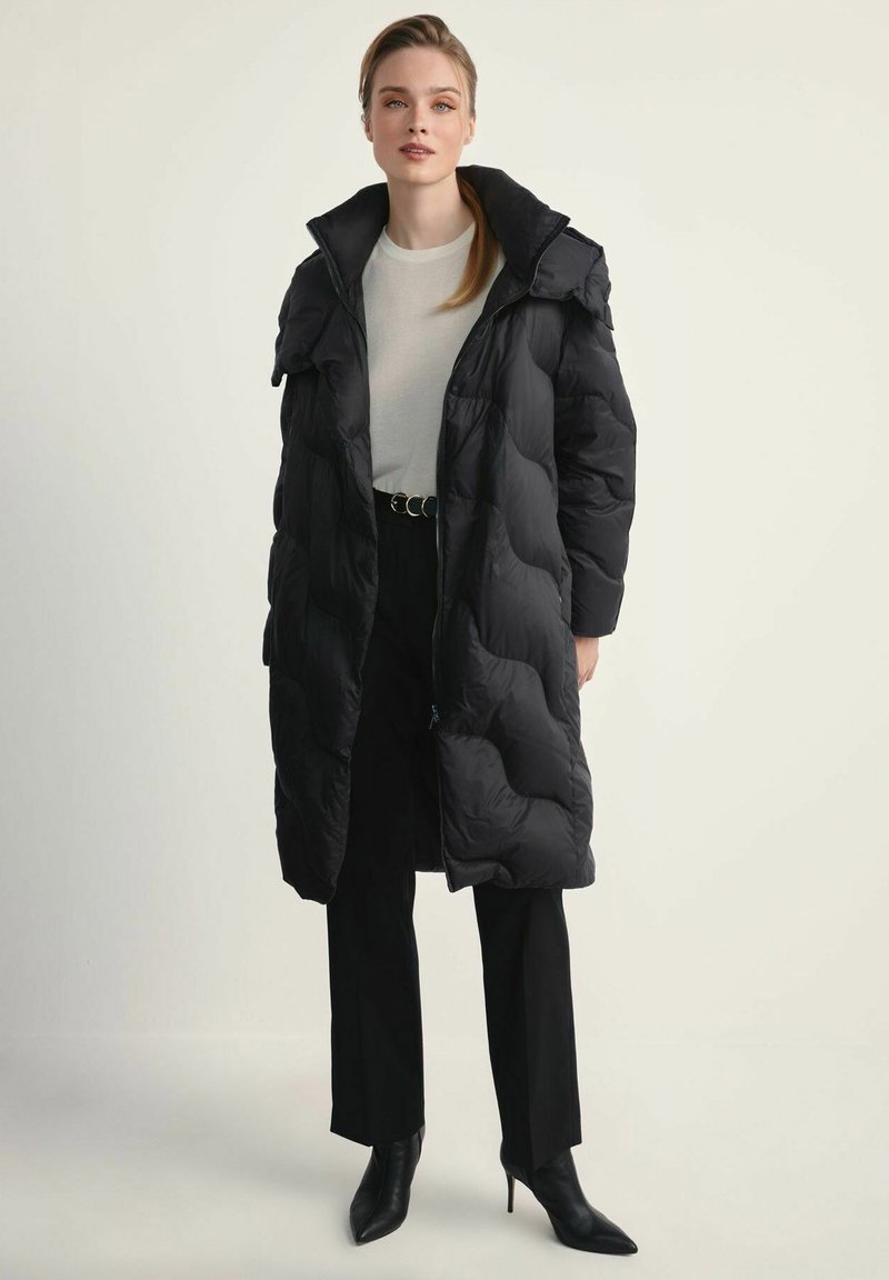 Czarna kurtka puchowa z kapturem, z pikowanym wzorem i zapięciem na zamek. Noszona na lekkiej bluzce, zestawiona z dopasowanymi spodniami i szpilkami.