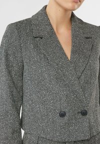 Marynarka w pepitkę w czarno-białym kolorze, z klapą z wycięciem, dwurzędowym zapięciem na dwa czarne guziki. Tkanina o fakturze.