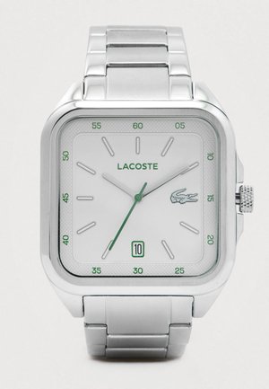 Montre en argent Lacoste avec un cadran carré, un cadran blanc, des accents verts, un affichage de la date à 6 heures et un bracelet en maillons métalliques.
