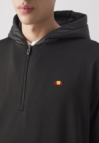Felpa nera con zip dal tessuto liscio, caratterizzata da un logo ricamato a contrasto in giallo, rosso e nero sul petto.