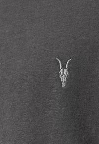 T-shirt grigia con un piccolo design di teschio di capra ricamato in grigio chiaro, con una consistenza liscia e una forma fitted.