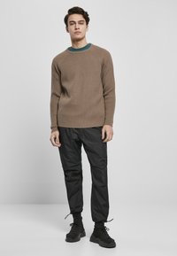Maglione a coste marrone chiaro con scollo rotondo, abbinato a pantaloni jogger neri e sneakers nere. L'outfit presenta uno stile casual.