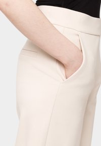 Beżowe spodnie taperowane o gładkiej fakturze, z bocznymi kieszeniami i wykrojem w talii. Minimalistyczny design z czystymi liniami.