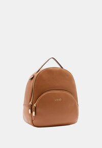 Zaino in pelle marrone con forma arrotondata, dotato di cerniere in tonalità oro e logo del marchio. Texture liscia e doppio scomparto con zip.