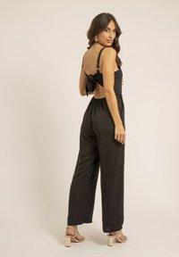 Combinaison noire avec jambes larges, bretelles ajustables et un détail de nœud à l'arrière. Fabriquée en tissu doux avec une coupe décontractée et des poches cachées.