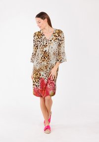 Vestido de estampado de leopardo con escote en V, mangas acampanadas de tres cuartos y un dobladillo floral rosa. Hecho de una tela ligera y fluida. Lleva sandalias rosas.