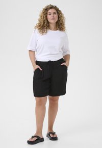 Shorts noirs texturés avec une taille élastique et un cordon de serrage. Associés à un t-shirt blanc ajusté et des tongs noires.