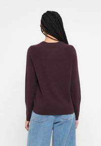 Pulover tricotat bordo cu mâneci lungi și decolteu rotund. Textură moale, croială lejeră, asortat cu blugi albaștri deschis, talie înaltă.