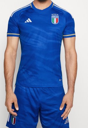 Camiseta de fútbol azul de Adidas con cuello en V, acentos dorados y el escudo de la selección nacional italiana. Tejido texturizado con patrones sutiles.