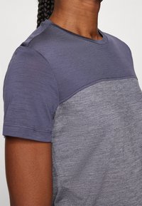 Koszulka z krótkim rękawem z kolorowym blokiem, ciemnoniebieską górą i jasnoszarym dołem, wykonana z miękkiego, teksturowanego materiału.