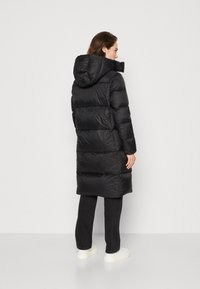 Black padded long coat with a hood, featuring horizontal quilted sections, a smooth texture, and a straight cut. Worn with dark pants and shoes.