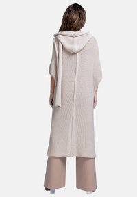 Długi, beżowy, dziany ponczo z kapturem, z teksturowanym wzorem i rozcięciami po bokach dla swobody ruchów.