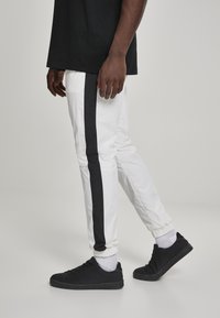 Hvite bukser med svart side stripe, elastiske mansjetter og en krøllete tekstur, kombinert med svarte sneakers og hvite sokker.