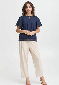 Top blu navy con rifiniture in pizzo e maniche corte, dotato di scollatura a chiave. Abbinato a pantaloni beige a gamba larga e tacchi marroni.
