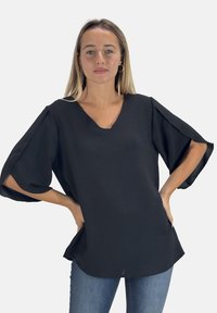 Zwarte, loszittende top met een v-hals, korte, uitlopende mouwen en een gestructureerde stof. Gecombineerd met blauwe jeans.