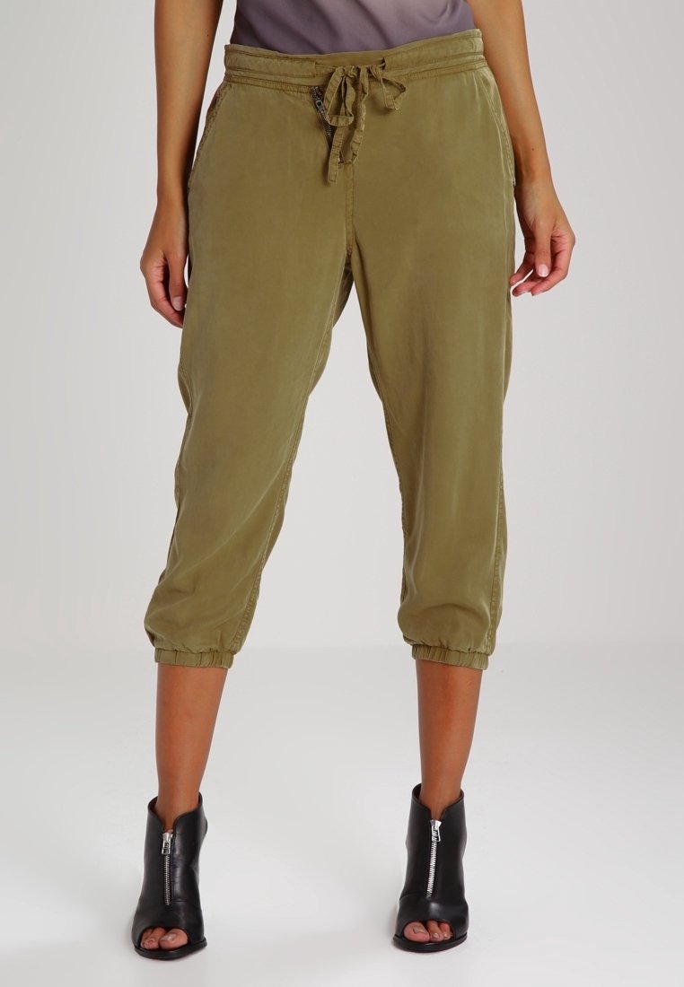 Mujer que lleva pantalones recortados en verde oliva con puños elásticos y cintura con cordón, combinados con botas de tobillo negras con punta abierta y cremalleras frontales.