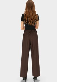 Luźne, ciemnobrązowe spodnie z elastycznym pasem i dwoma tylnymi kieszeniami, zestawione z czarną dopasowaną bluzką i butami na wysokim obcasie.