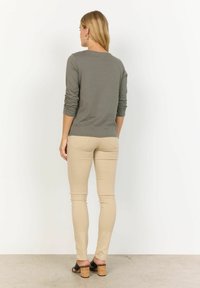 Khaki pikkade varrukatega särk, mis on kombineeritud beežide kitsaste pükstega ning mustade kontsadega sandaalidega korkaktsentidega. Kangas tundub pehme ja kerge venivusega.