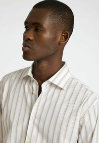 Biała koszula na guziki z pionowymi paskami w odcieniach beżu i jasnobrązowym. Posiada klasyczny kołnierzyk i gładki, strukturalny materiał.