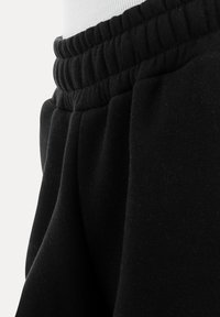 Close-up van een zwarte elastische tailleband en geplooide stof van een paar casual joggingbroeken.