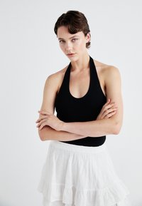 Fekete, nyakpántos bodysuit, amelyet fehér, rétegezett szoknyával párosítottak, mivel az eyelet hímzés díszíti. Sima anyag, testhez simuló dizájn és nyitott dekoltázs.