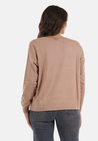 Maglione a maglia marrone chiaro con vestibilità rilassata, scollo a forma di U e orlo a coste. La parte posteriore presenta un piccolo dettaglio decorativo all'altezza dello scollo.