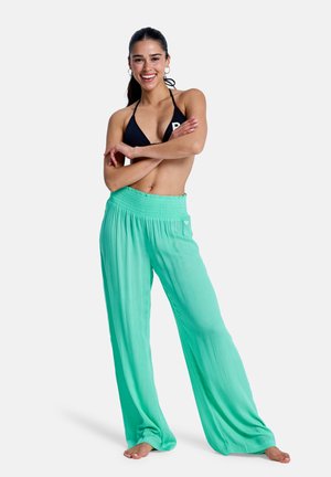 Lyse, mintgrønne bukser med vide ben og smocktalje; modellen bærer en sort bikinitop, smiler og har langt hår sat tilbage.