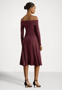 Bordo obleko z odkritimi rameni, dolgimi rokavi, oprijetim trupom, razširjenim krilom in gladko teksturo. Kombinirano s črnimi sandalami z visoko peto.